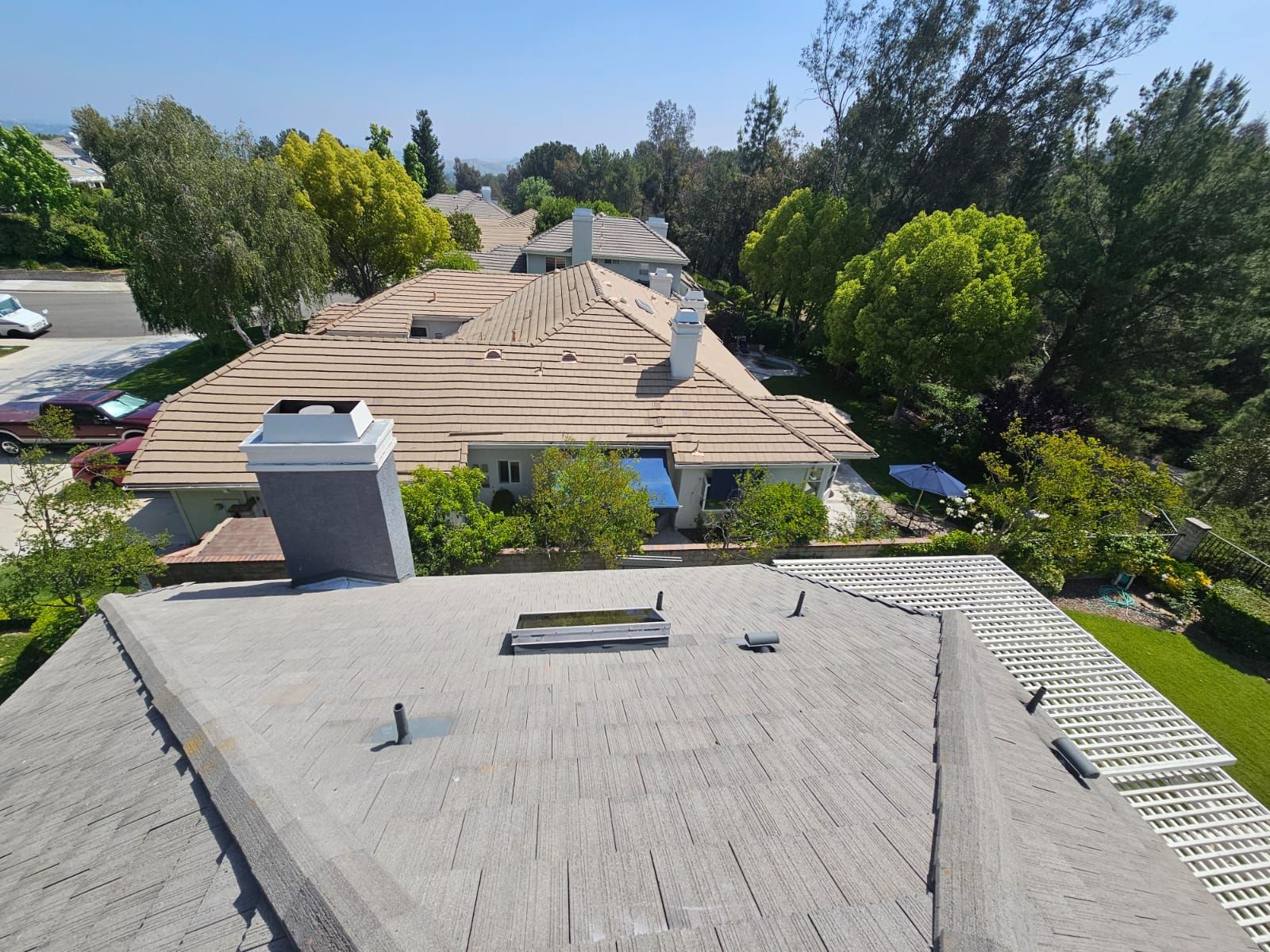 Overhead view of multiple houses with rooftops of varying colors and trees. Sunny day.
