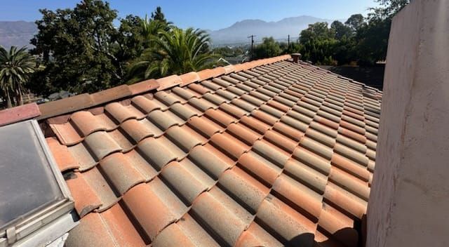 Clay tile roof with a view of trees and mountains under a blue sky.