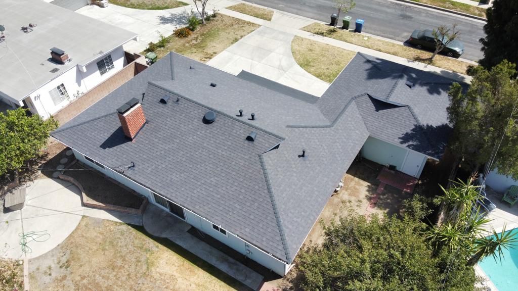 Aerial view of a house with a dark grey shingle roof, a brick chimney, and a circular driveway.
