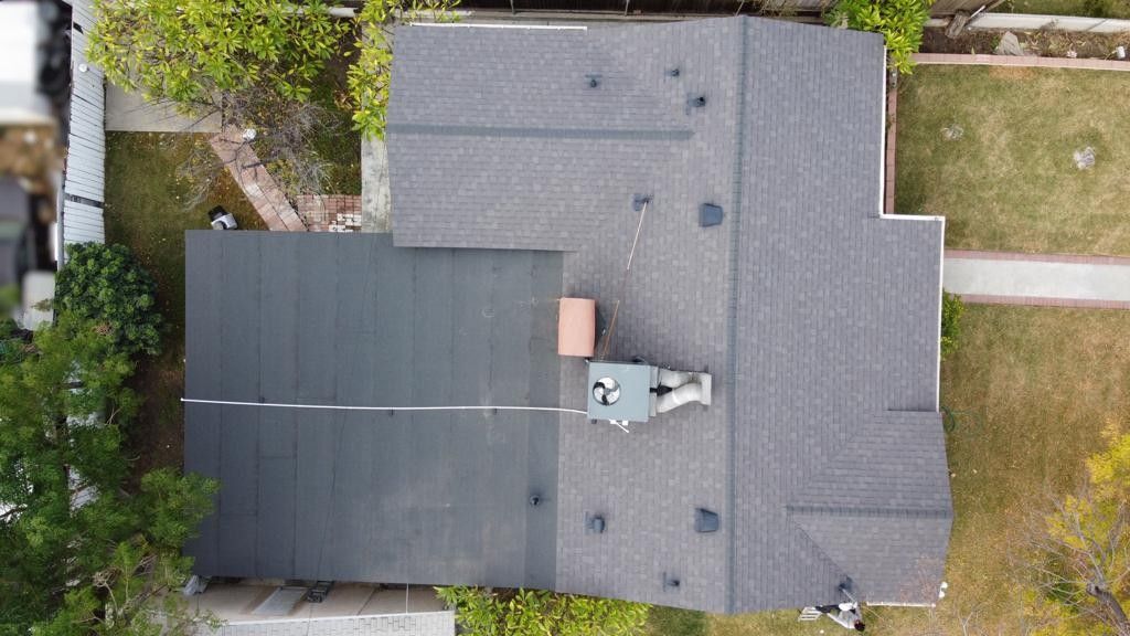 Overhead view of a house with a dark gray shingled roof, surrounded by trees and grass.