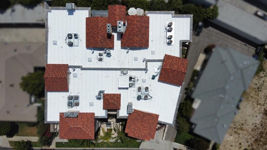 Overhead view of a building with a white flat roof, red tile sections, and rooftop HVAC units.