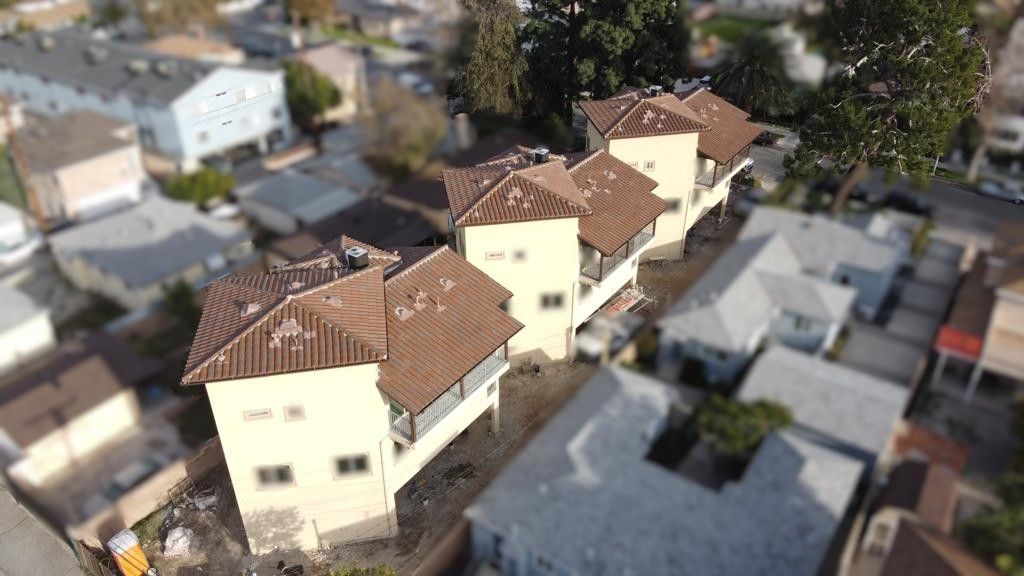 Aerial view of a row of light-colored townhouses with brown roofs, in a residential neighborhood.