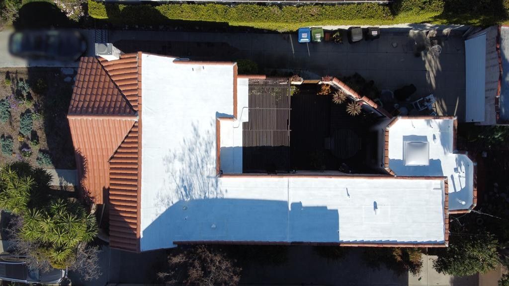Aerial view of a house with white flat roofs, brown tile roof, and a pergola in the yard.