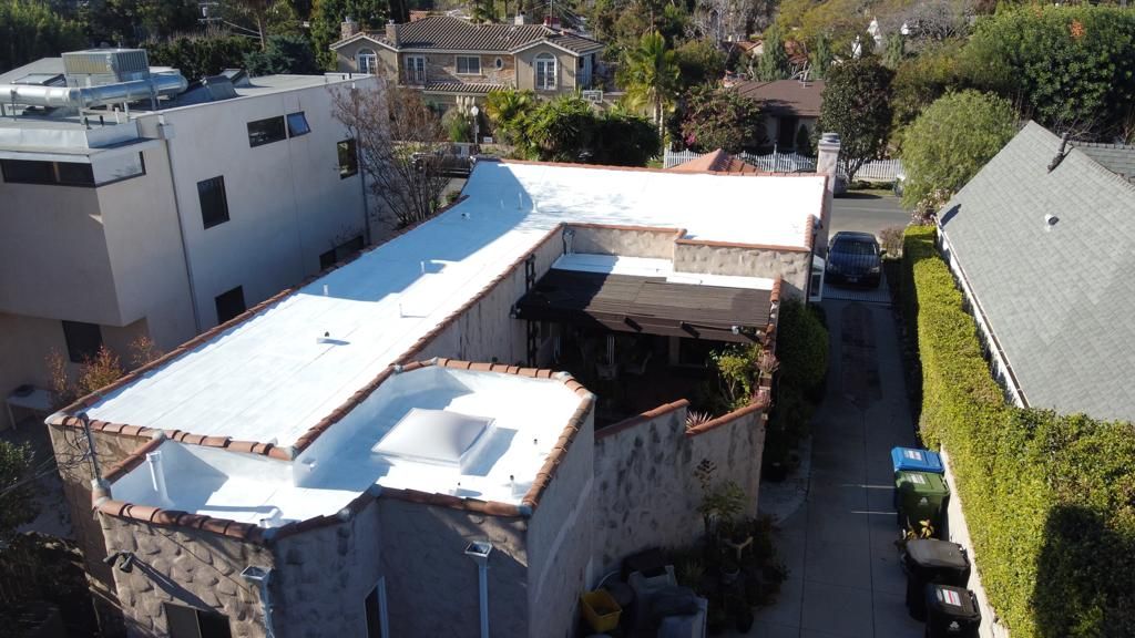 Aerial view of a white-roofed house with a car parked in an alleyway.