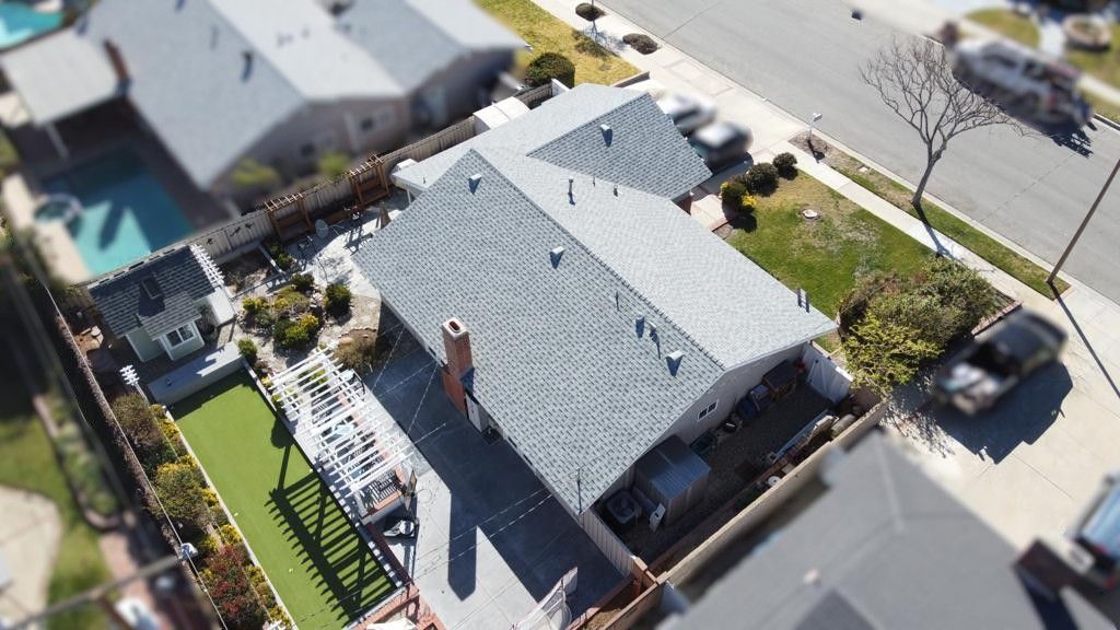 Aerial view of a house with a gray roof and backyard, including a pool and patio.