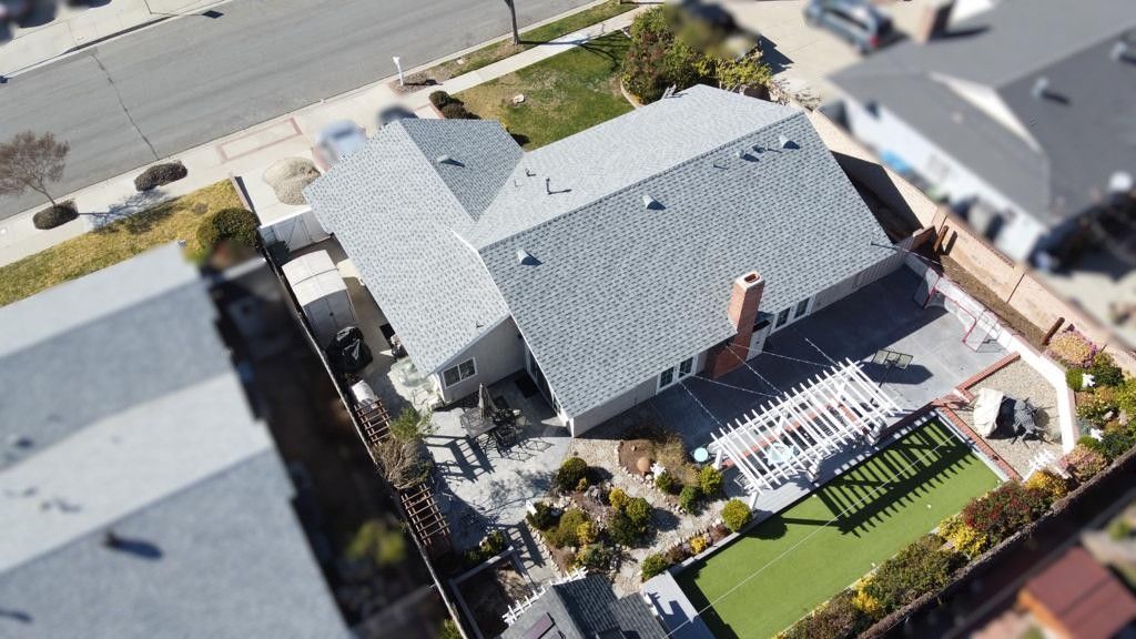 Aerial view of a house with a grey roof, chimney, and backyard patio.