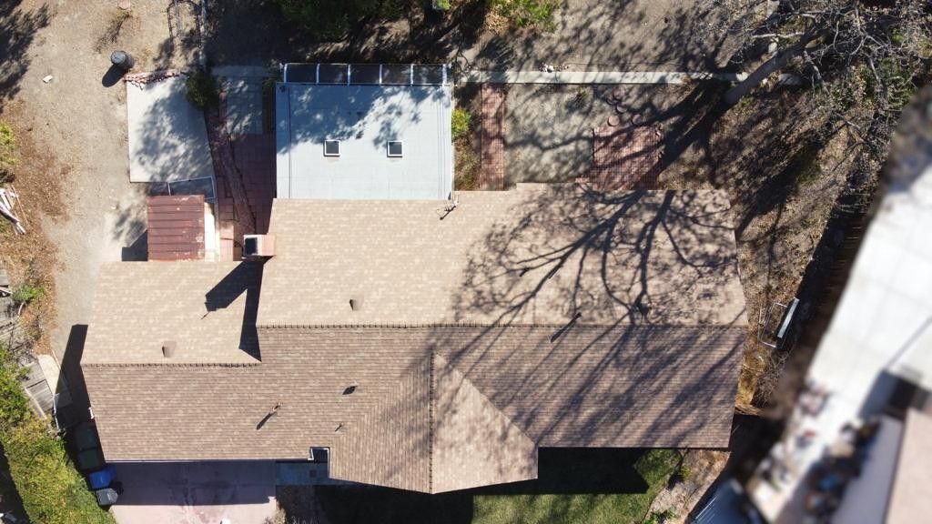 Aerial view of a house with brown roof and attached structures, surrounded by trees and grass.