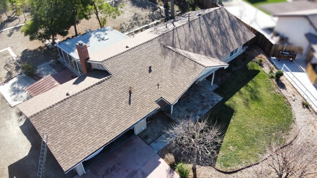 Aerial view of a house with a brown roof, driveway, and surrounding green grass.