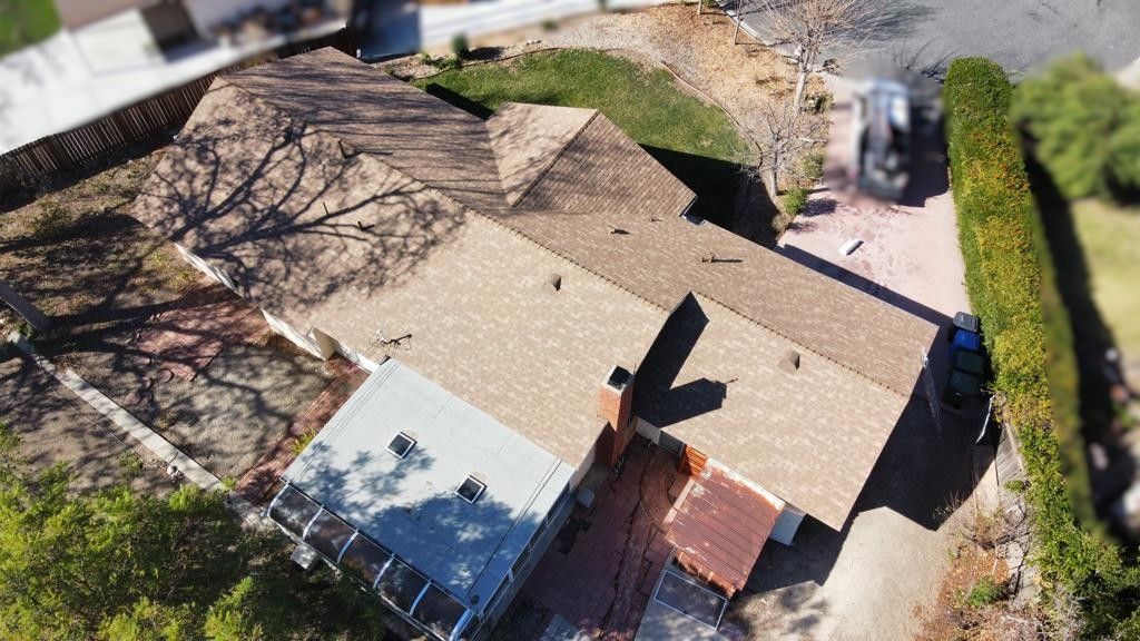 Aerial view of a house with brown roof, red brick chimney, and a car parked in the driveway.