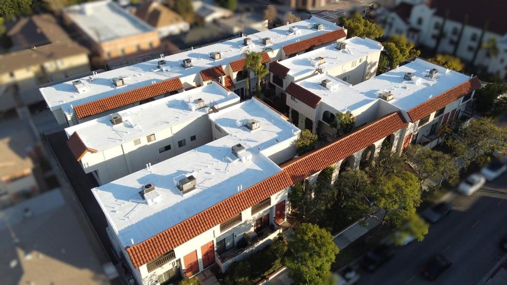 Multi-unit residential complex with white walls, terracotta roofs, and surrounding trees.