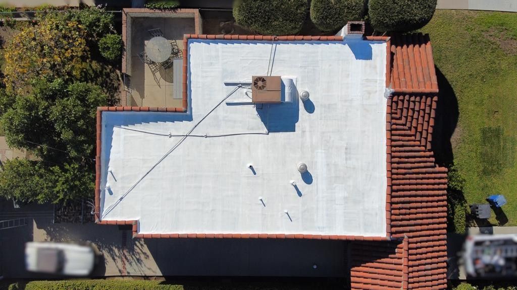 Overhead view of a house with white flat roof, red tile trim, and an attached patio.