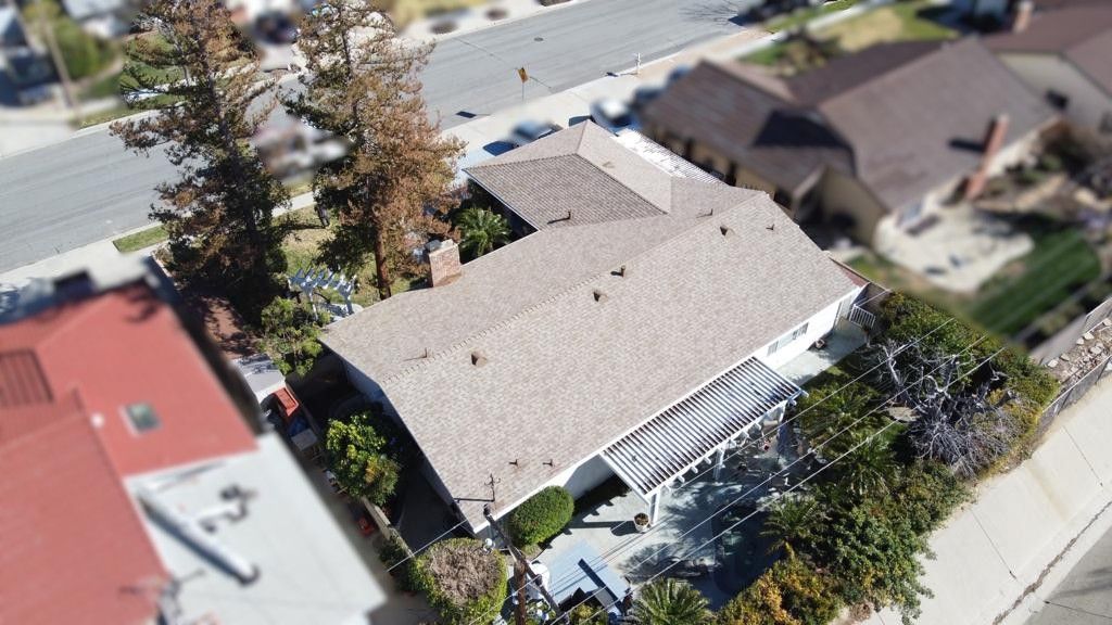 Aerial view of a house with a brown roof, surrounded by trees and other buildings.