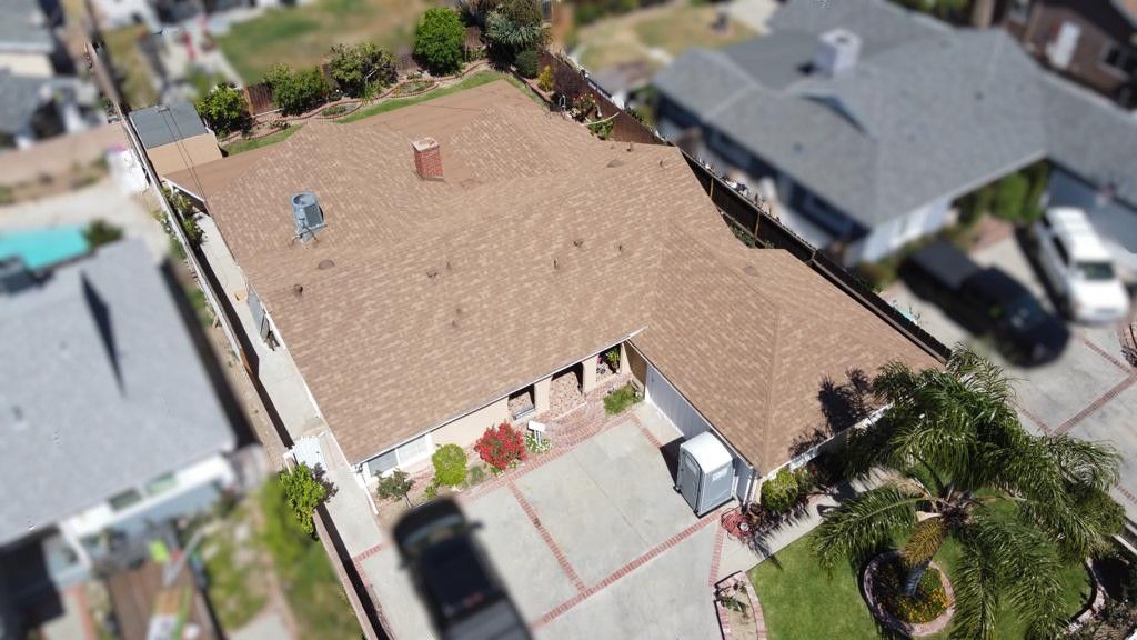 Aerial view of a house with brown roof, driveway, and green lawn, in a suburban neighborhood.