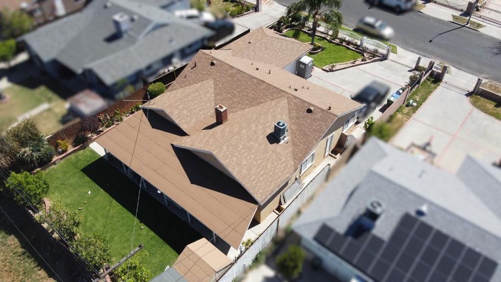 Aerial view of a brown roofed house with green lawn, in a residential neighborhood.