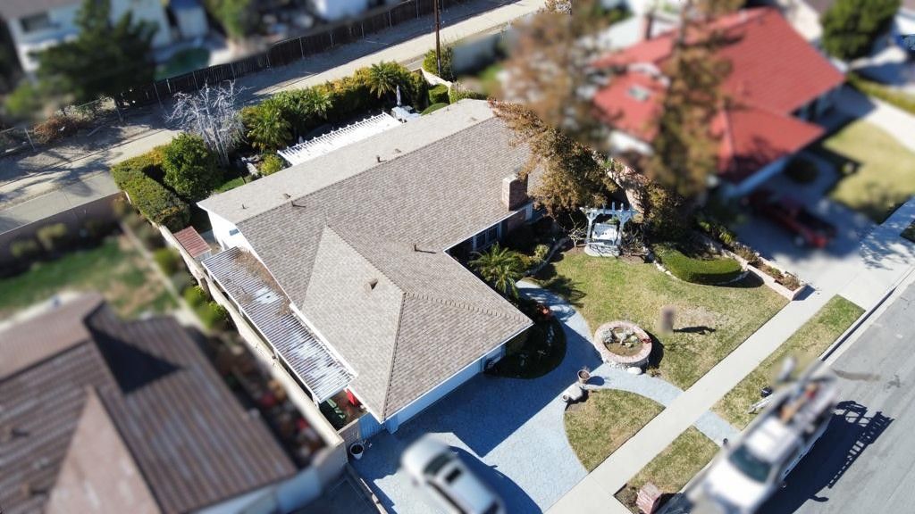 Aerial view of a house with a light brown roof, front yard, driveway, and street.