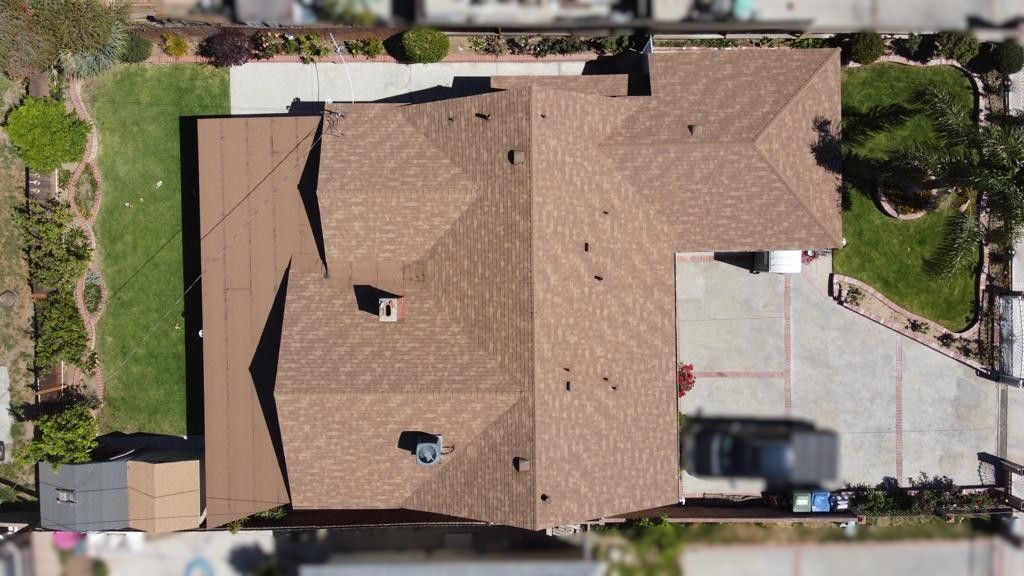 Overhead view of a house with a brown roof, green yard, and driveway; a van is parked in the drive.