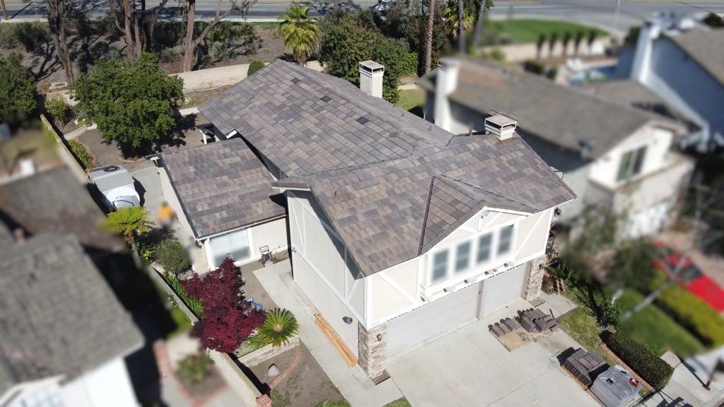 An aerial view of a beige house with a gray roof, two-car garage, and landscaping.