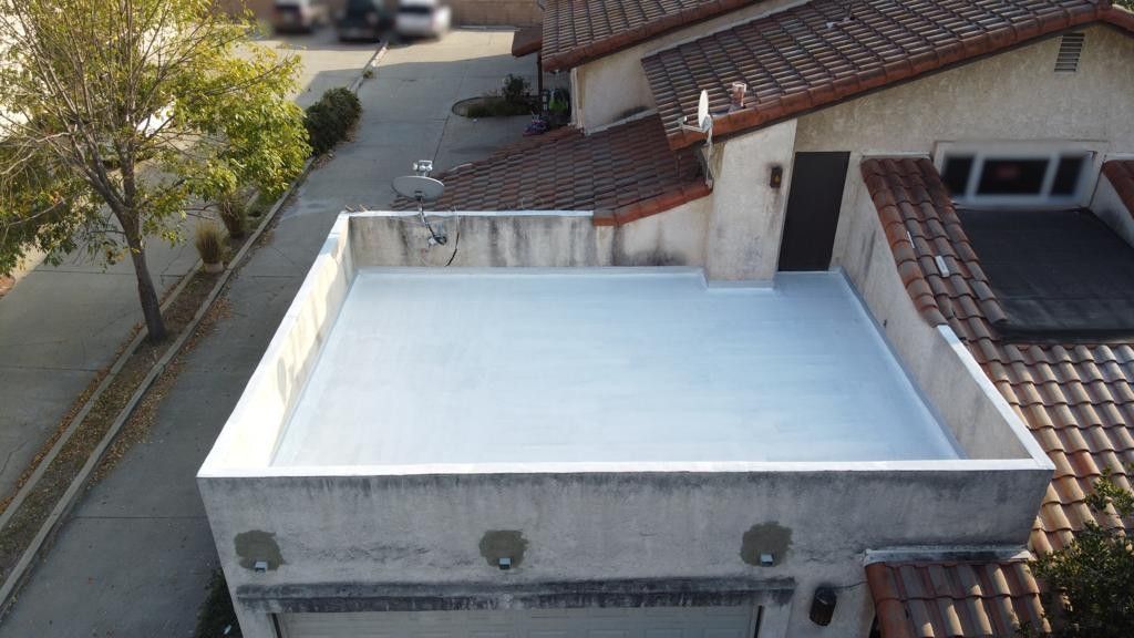Flat roof on a building, freshly coated in white. Street and vehicles in the background.