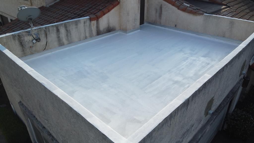 Flat rooftop, freshly coated in light gray sealant, surrounded by concrete walls.