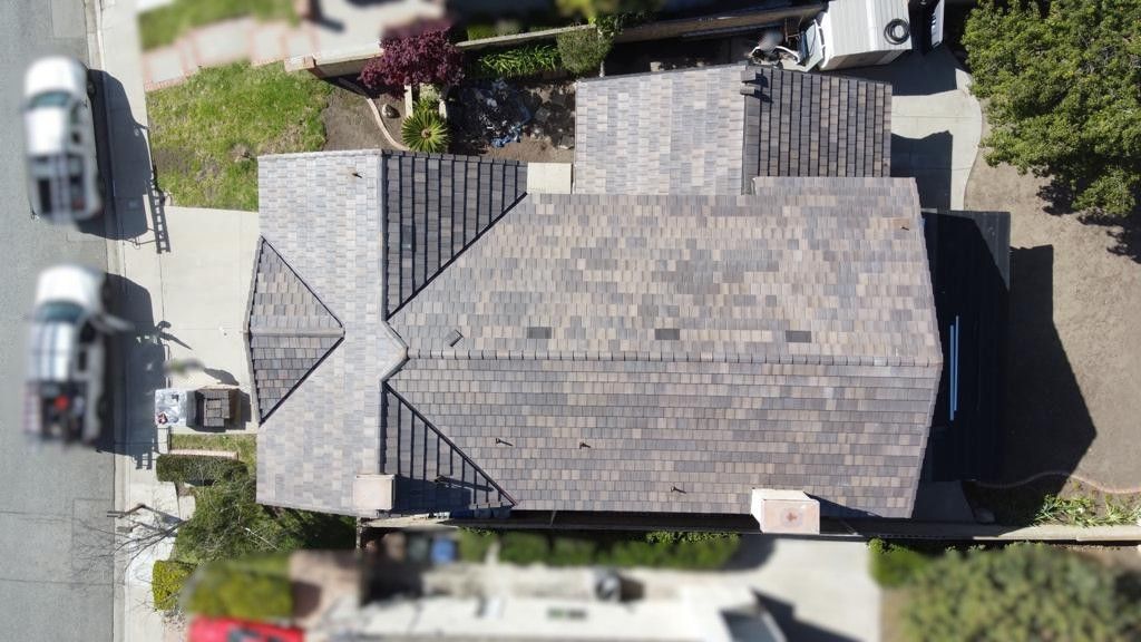 Overhead view of a house with gray roof, cars on street, and green landscaping.