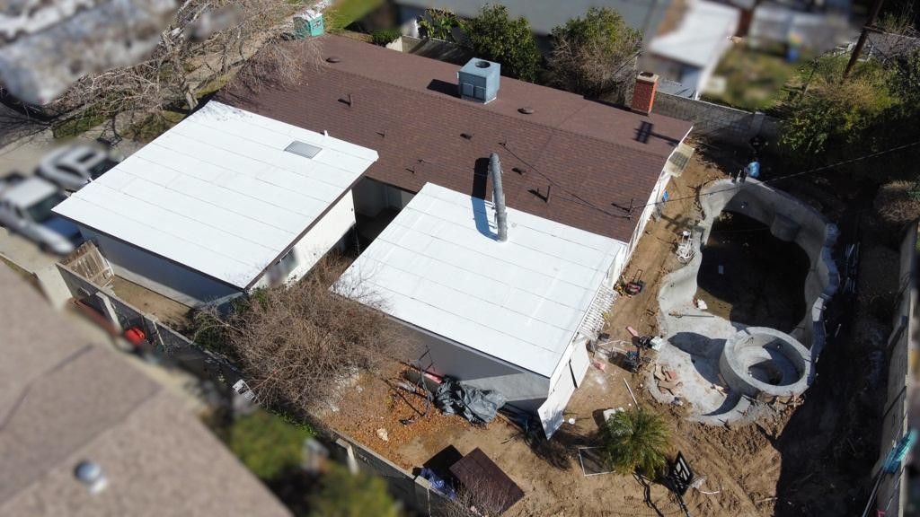 Aerial view of a house with a brown roof, white sheds, and a pool under construction.