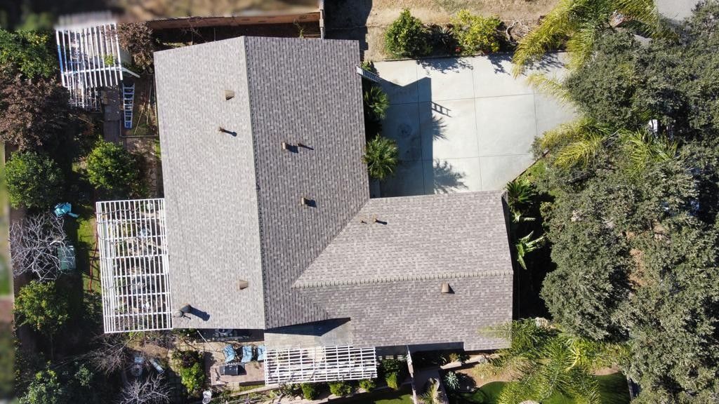 Overhead view of a house with a grey roof, surrounded by trees and a concrete driveway.