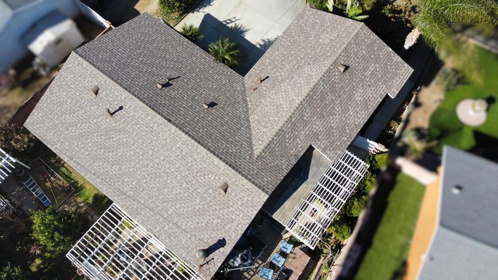Overhead view of a house with gray shingle roof and backyard with a pergola and green grass.