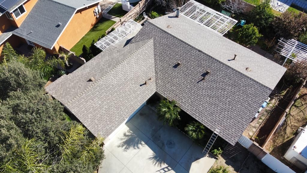 Aerial view of a house with a grey roof, driveway, and surrounding trees.
