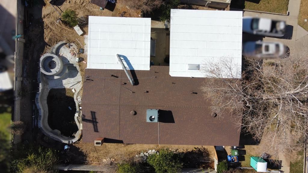 Overhead view of a house with a dark brown roof, white square roofs, and a pool next to it.