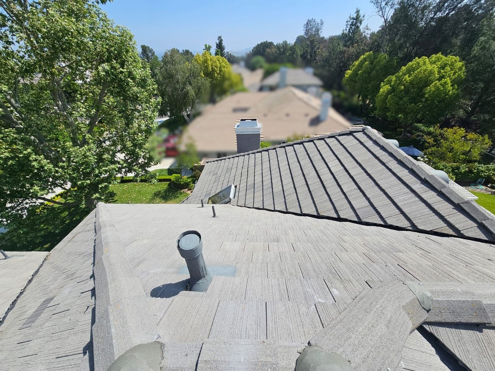 View from a rooftop, looking over other houses. Gray roof tiles, blue sky.