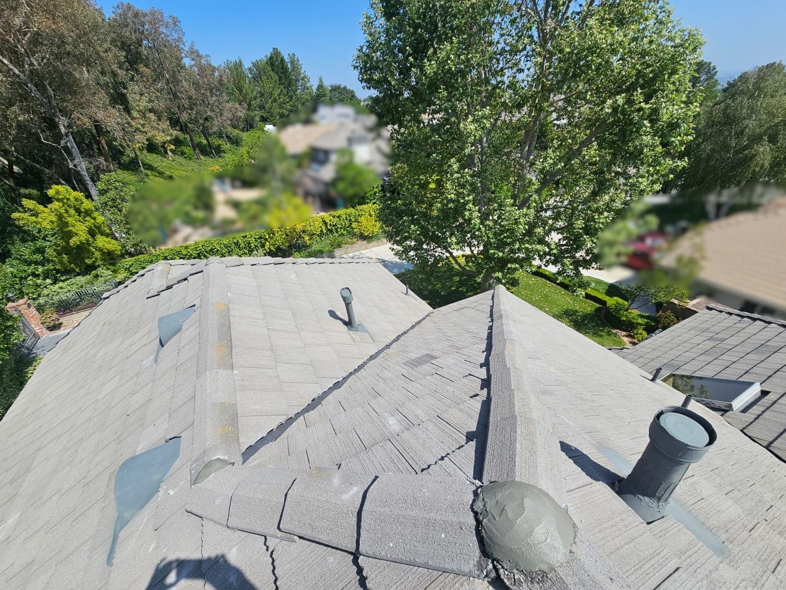 Gray roof with vents, trees and houses in the background on a sunny day.