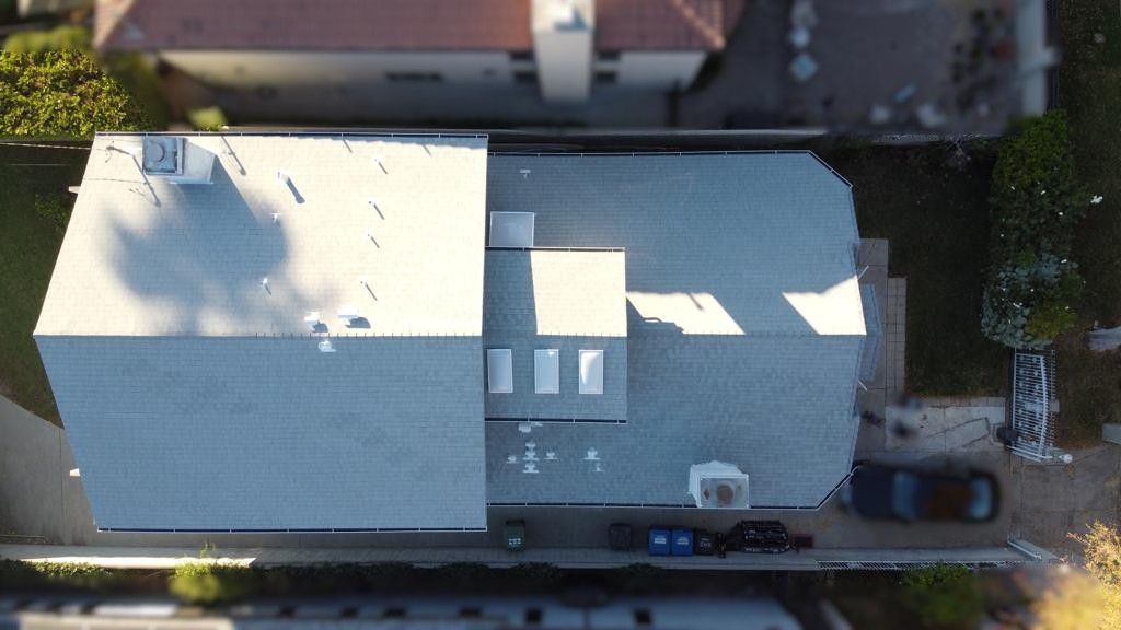 Overhead view of a house with a gray roof, a black car parked in the driveway, and green bushes.