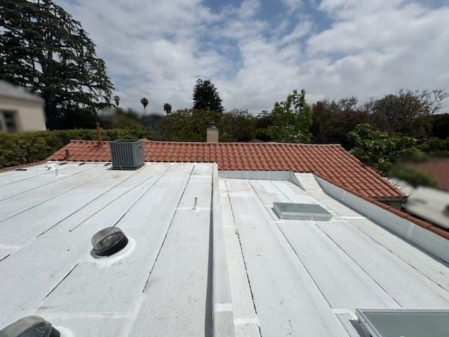 A roof with white flat sections, orange tile, and vents, under a cloudy sky.