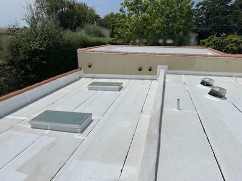 Flat roof with two skylights, vents, and a rectangular parapet wall on a sunny day.