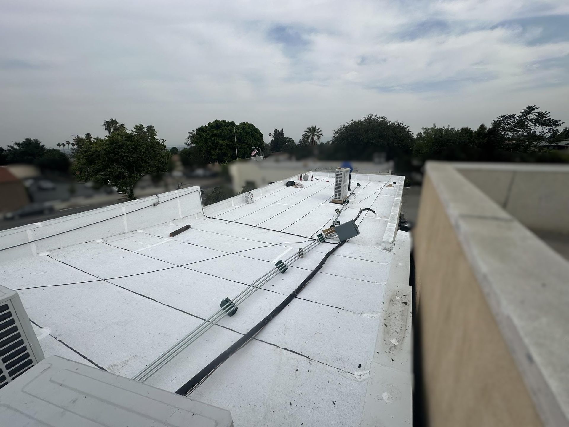 White rooftop with utility lines, trees, and a cloudy sky in the background.