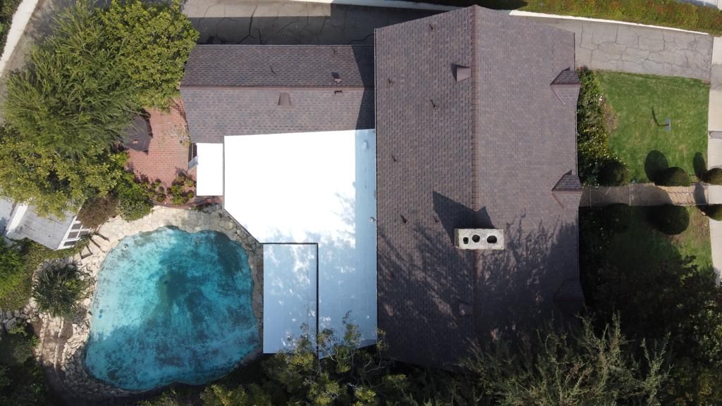 Overhead view of a house with a pool, brown roof, and green lawn.
