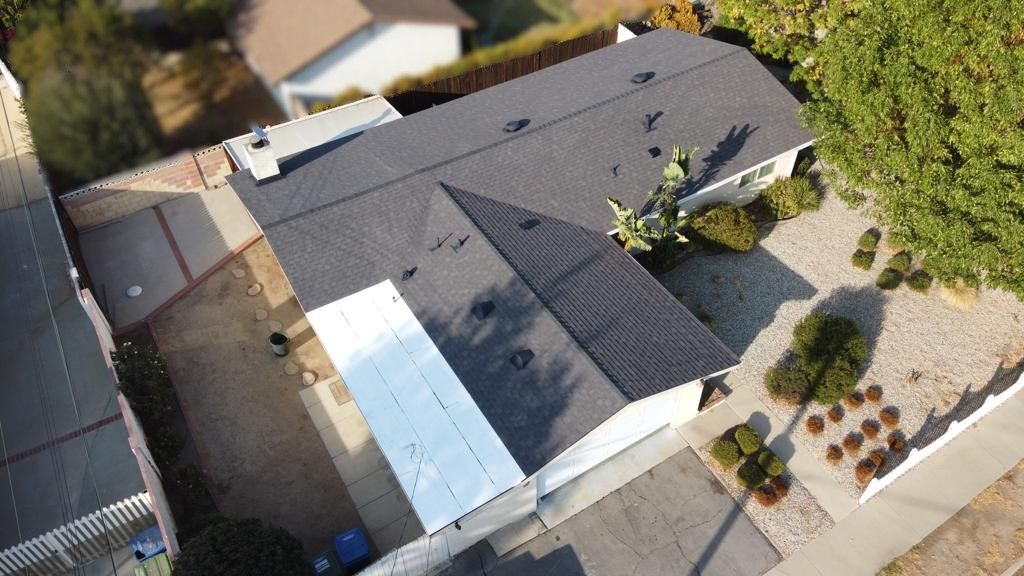 Overhead view of a house with a dark roof, white siding, and a driveway surrounded by greenery.