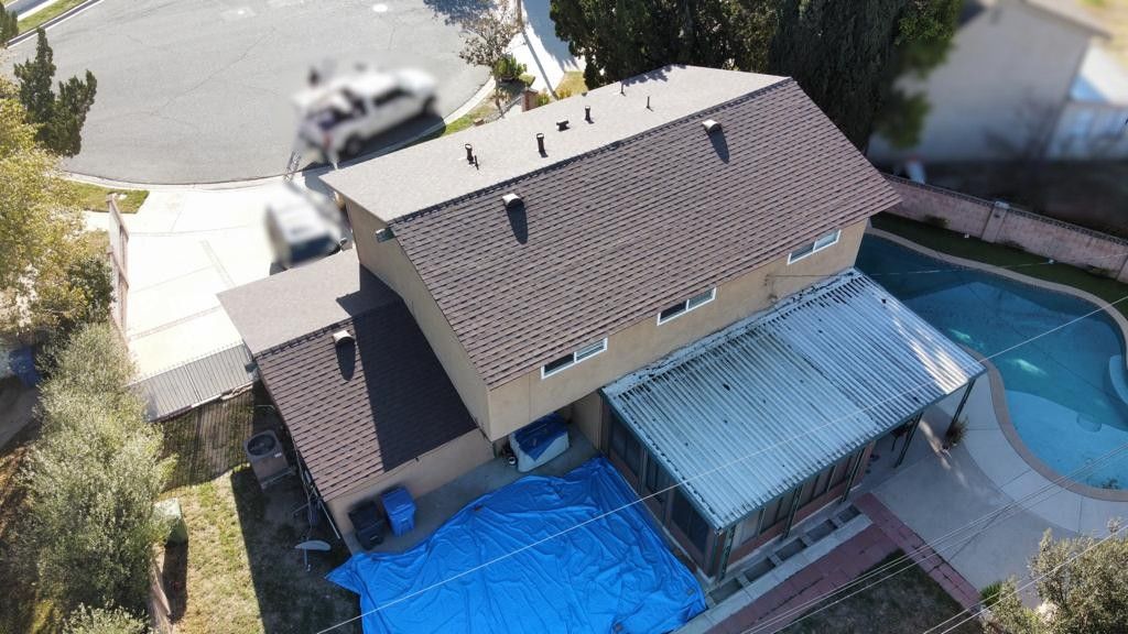 Aerial view of a two-story house with a pool, brown roof, and blue tarp covering a patio.