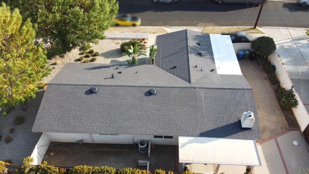 Overhead view of a gray-roofed house with a white extension, a backyard, and a street in the background.