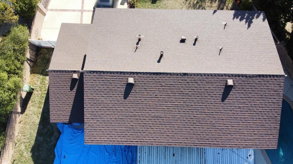 Overhead view of a brown-shingled roof on a house with multiple vents.