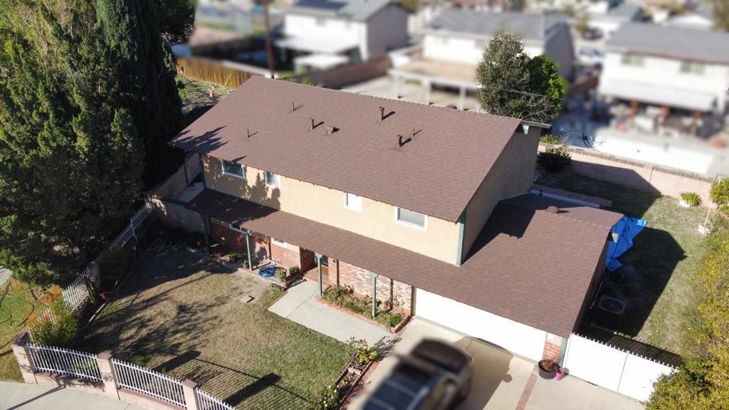 Aerial view of a two-story beige house with a brown roof and a black car in the driveway.