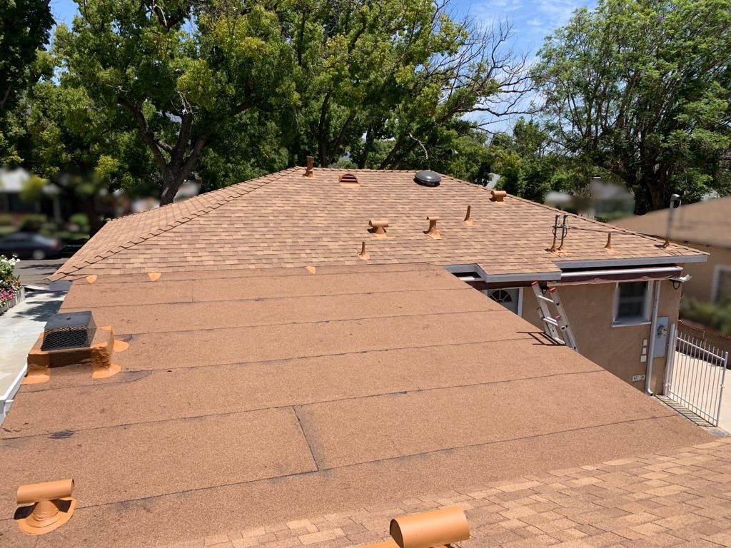 Brown roofing with some shingles in place, sunlight, trees in the background.