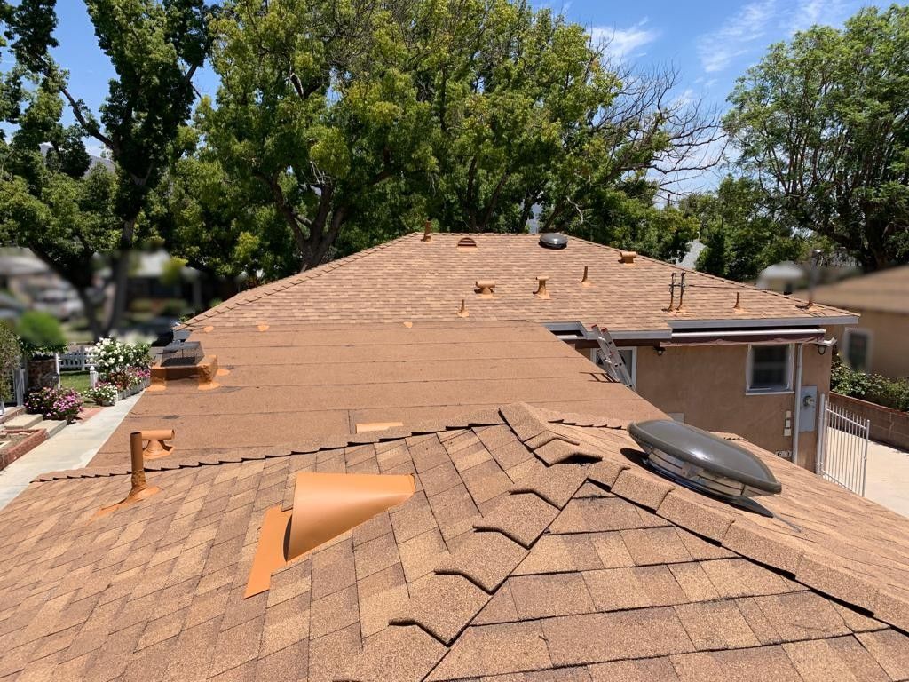 Brown shingled rooftops with vents, viewed from above, under a partly cloudy sky.
