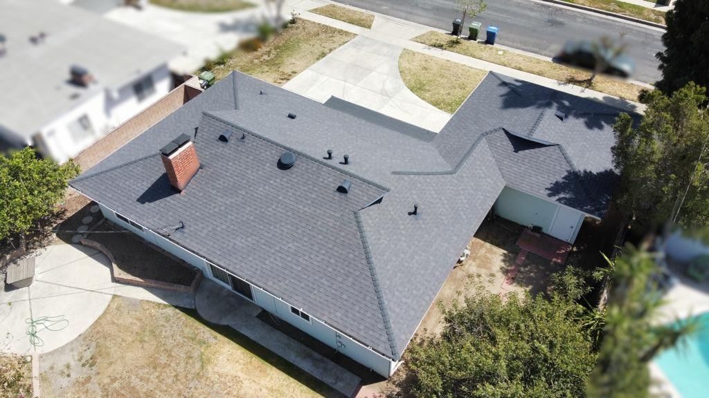 Aerial view of a house with a dark gray roof, driveway, and a small front yard with trees.