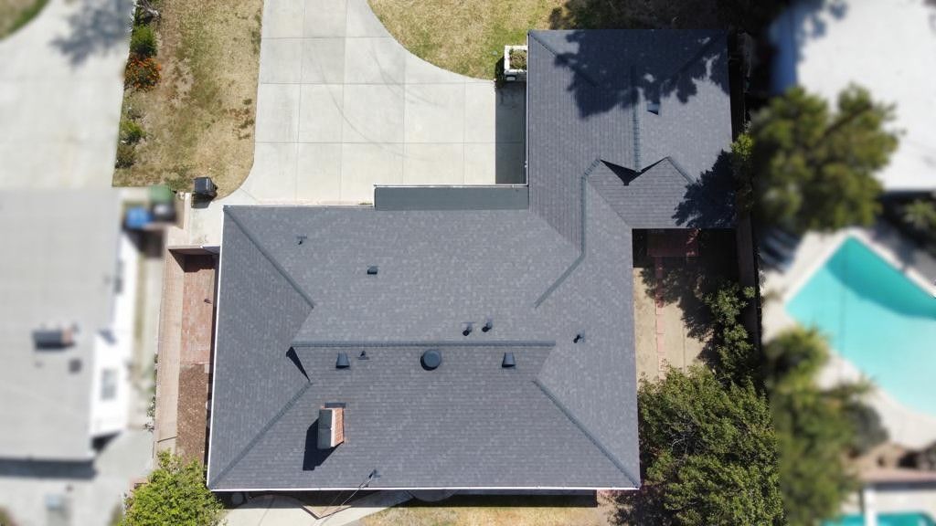 Overhead view of a gray shingled house with a driveway, surrounded by lawn and a swimming pool.