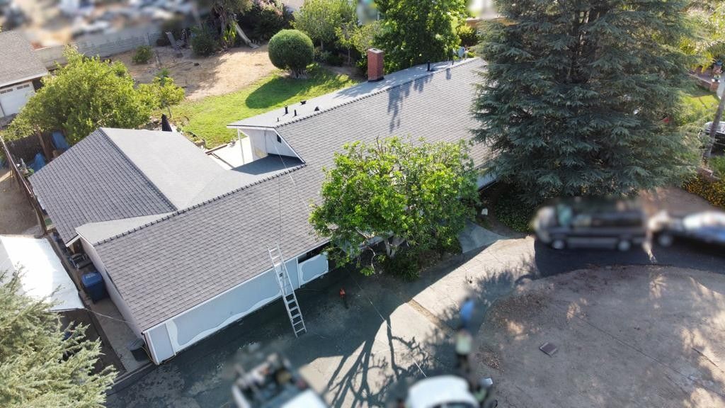 Aerial view of a house with a gray roof, green trees, and vehicles in the driveway.