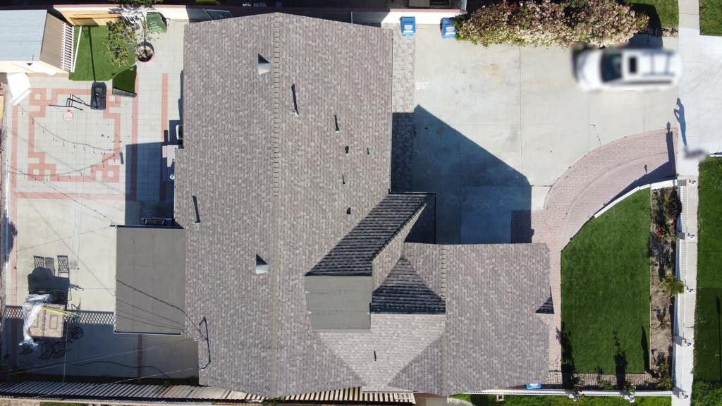 Overhead view of a house with a gray shingle roof, driveway, and a red-brick patio.