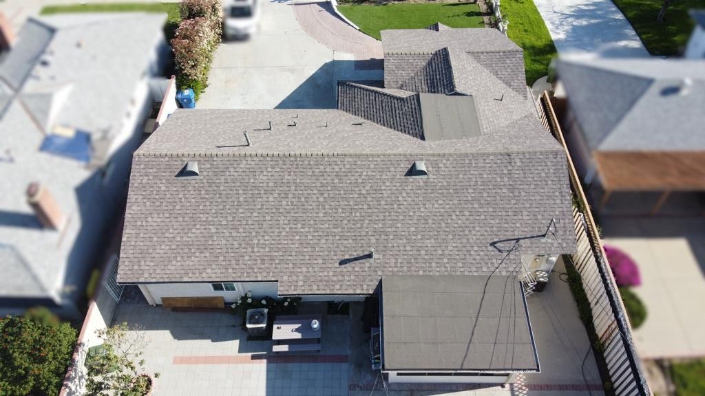 Overhead view of a house with a gray roof, driveway, and yard in a suburban neighborhood.