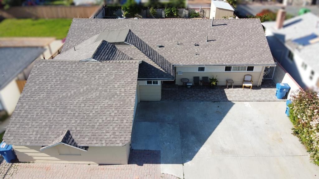 Aerial view of a house with a grey roof, driveway, and blue trash bins.