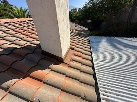 Terracotta roof tiles surrounding a white chimney, next to a corrugated metal roof.